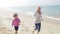 Grandmother And Granddaughter Running Along Beach Together