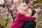 Grandmother and granddaughter together, hugging and laughing in a Flowering apricot garden. Family outdoors lifestyle