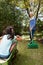 Grandmother holding rake while looking granddaughter sitting in wheelbarrow