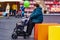 Grandmother holds an empty pram and  green inflatable balloon and looks forward behind baby. Side view.