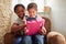 Grandmother Sitting In Chair With Granddaughter Watching Movie On Digital Tablet Together