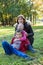 Grandmother with two grandchildren sitting on green grass in autumn park