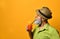 Grandpa in hat, green shirt, sunglasses. Twisting mustache, holding glass of fresh squeezed juice, posing on orange background