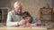 Grandpa helps a grandson with homework. Elderly man helps a young fat child to do homework. Home comfort, family idyll