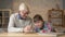 Grandpa helps a grandson with homework. Elderly man helps a young fat child to do homework. Home comfort, family idyll