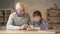 Grandpa helps a grandson with homework. Elderly man helps a young fat child to do homework. Home comfort, family idyll