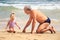 Grandpa Little Girl Sit on Wet Sand Look at Shell by Surf
