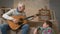 Grandpa plays for his grandson on guitar, music. A young fat guy is sitting on the haven with his grandfather. Teaches