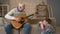 Grandpa plays for his grandson on guitar, music. A young fat guy is sitting on the haven with his grandfather. Teaches