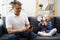 Grandpa sitting on sofa and using smartphone, little granddaughter shouting through megaphone to him to stop