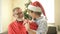 Grandpa wearing a Santa hat makes a Christmas present to his teenage grandson. The boy is delighted with the gift