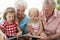 Grandparents And Grandchildren Reading Book On Garden Seat