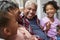 Grandparents Relaxing On Sofa At Home With Granddaughters