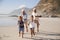 Grandparents Running Along Beach With Grandchildren On Summer Vacation