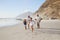 Grandparents Running Along Beach With Grandchildren On Summer Vacation