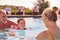 Grandparents Teaching Granddaughter To Swim On Family Summer Holiday In Pool 