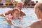 Grandparents Teaching Granddaughter To Swim On Family Summer Holiday In Pool 