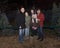 Grandparents and three granddaughters outside standing in front of Christmas trees