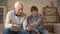 The grandson teaches grandfather to play the console game. Elderly man is learning how to play a video game, he does not