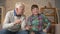 The grandson teaches grandfather to play the console game. An elderly man is learning how to play a video game. Video