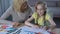 Granny stroking granddaughter head, cute girl painting house with colored pencil