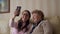 Granny and young girl making self photos on mobile or smart phone while sitting on sofa or couch at home. Happy ladies