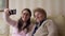 Granny and young girl making self photos on mobile or smart phone while sitting on sofa or couch at home. Happy ladies