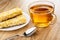 Granola bar with corn flakes, puffed rice, coconut and chocolate in saucer, spoon, cup with tea on wooden table