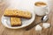 Granola bars with chocolate in saucer, sugar, cup with black coffee, spoon on wooden table