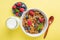 Granola with summer berries and bottle of milk on yellow background