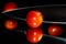 Grape tomatoes against a black background being sliced with a sharp knife on a highly reflective surface. Vibrant colors