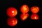 Grape tomatoes against a black background being sliced with a sharp knife on a highly reflective surface. Vibrant colors.