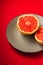 Grapefruit two half on grey plate, tropical creative minimal food fruit concept, on vibrant red background