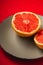 Grapefruit two half on grey plate, tropical creative minimal food fruit concept, on vibrant red background