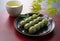 Grass dumplings and green tea placed on a red Japanese tray