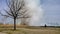 Grass fire prescribed burn for prairie restoration with firefighter and tree in foreground