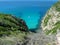 Grass on a rocky cliff with a white boat moored on blue sea waters in Formentera, Spain