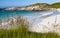 Grass by a sandy beach, a distant lighthouse and gren hills