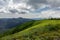 A grassy mountain top with a sky filled with clouds.