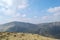 A grassy, rock strewn mountain top with other mountains beyond