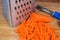 Grated carrot large slices against the kitchen grater close-up