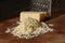 Grated italian parmesan cheese on wooden chopping board with a block of parmasan and a grater in the background. Close up photo