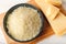 Grated parmesan or grana padano in a ceramic bowl and wedge of hard cheese on a brown cutting board. Delicious ingredient for