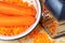 Grated and whole carrots in the metal bowl with stainless steel grater on the kitchen table close-up