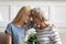 Grateful aged mother holding flowers touches foreheads with adult daughter