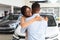 Grateful Black Wife Embracing Husband After Buying New Car In Dealership Showroom