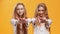 Gratitude concept. Two young redhead twin sisters touching chests and reaching hands to camera, orange background