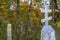 Grave monument in the form of an orthodox silver cross. Autumn graveyard background