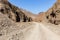 Gravel dirt road through rocky limestone Hajar Mountains and cliffs in United Arab Emirates, barren desert vegetation