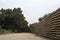 Gravel path in a clearing of an industrial complex that leads to a gate and a group of houses bordered by trees on a cloudy day